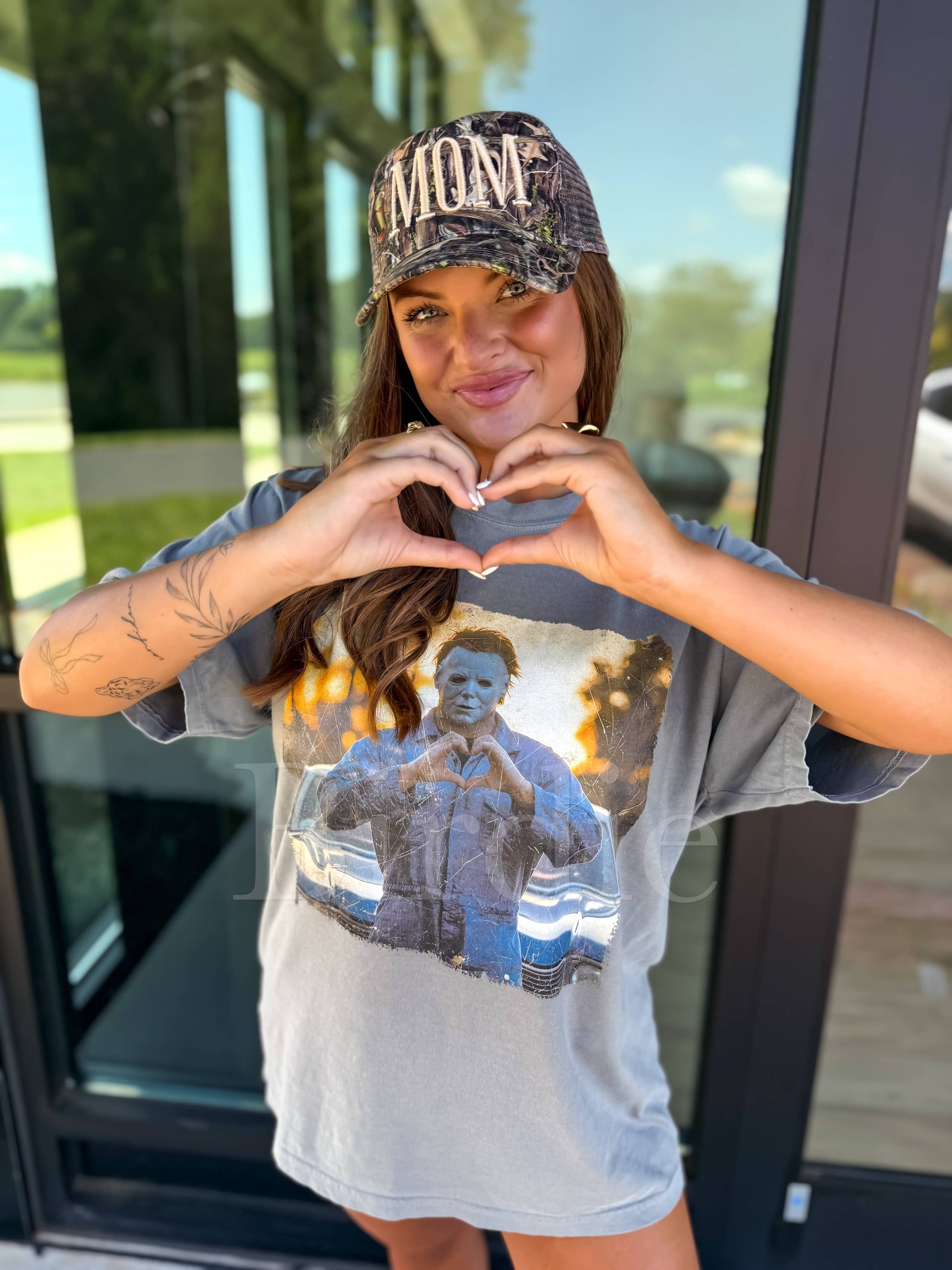 Woman wearing a graphic t-shirt and cap, making a heart shape with her hands.
