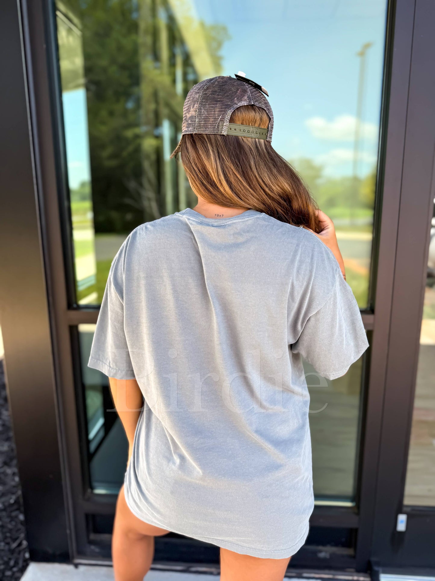 Person wearing a gray t-shirt and cap standing in front of a glass door.