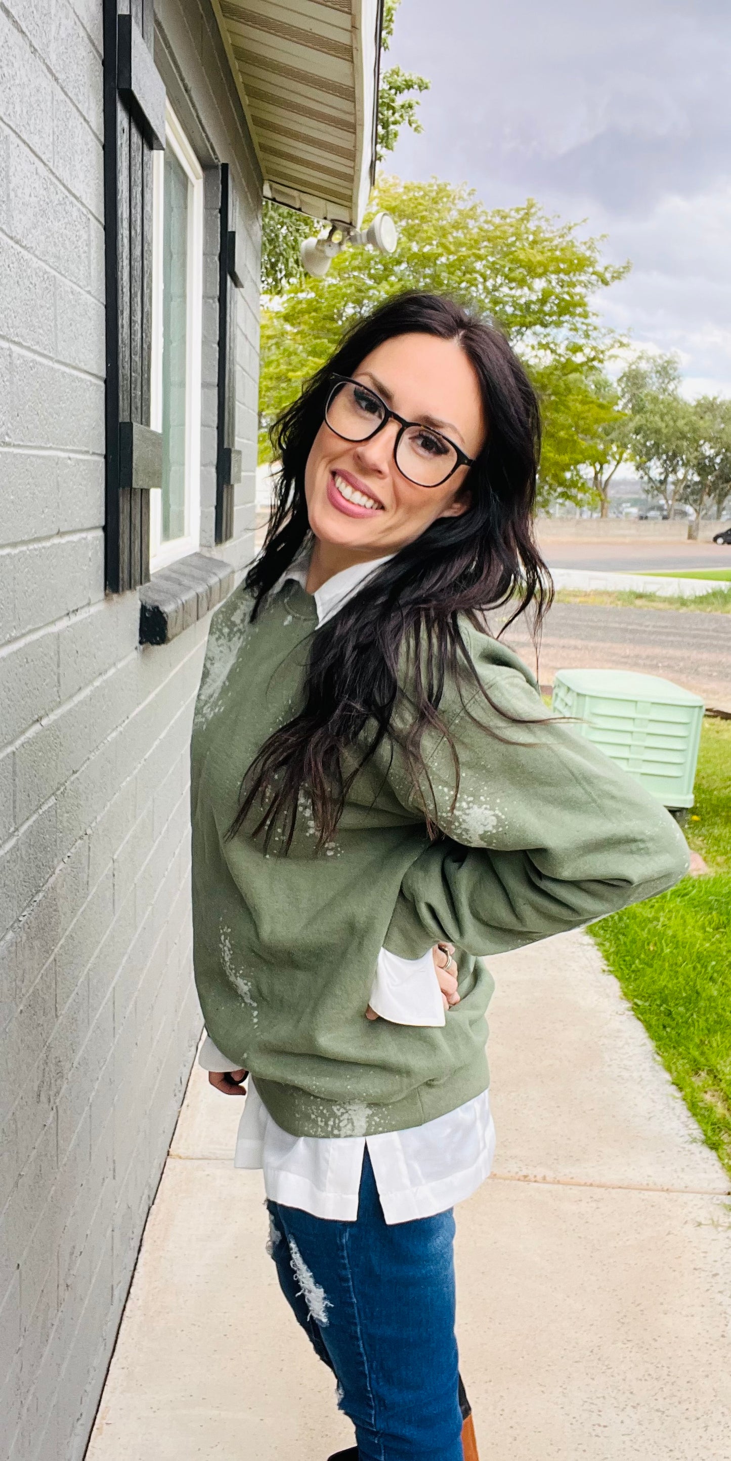 Woman wearing a green bleached sweater and blue jeans standing outside a building.