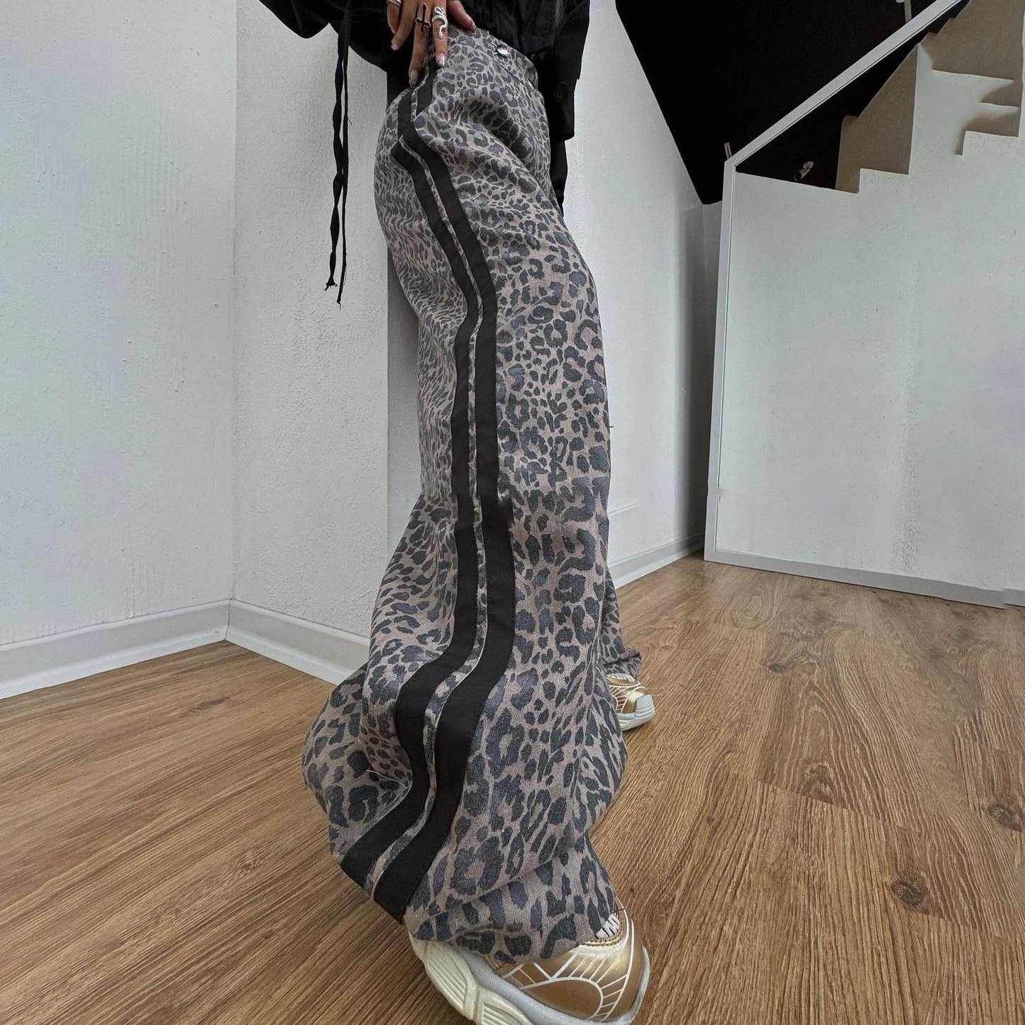 Person wearing leopard print pants with black stripes indoors on a wooden floor.