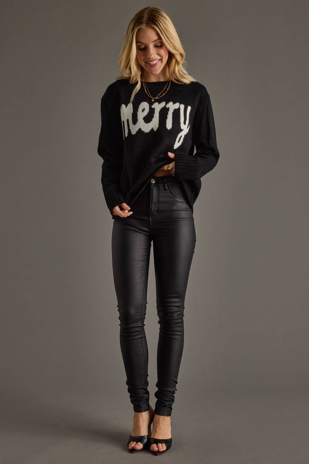 Woman wearing a black sweater with 'merry' text and black pants on a gray background