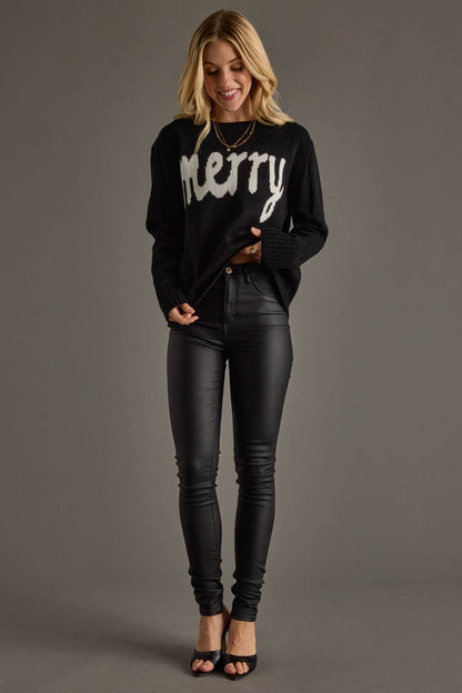 Woman wearing a black sweater with 'merry' text and black pants on a gray background