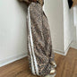 Person wearing leopard print pants with white stripes standing against a plain wall.