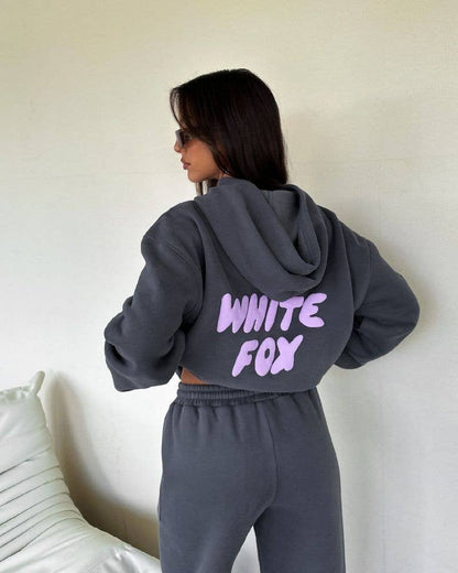 Person wearing a gray hoodie with 'White Fox' text on the back, standing against a white wall.
