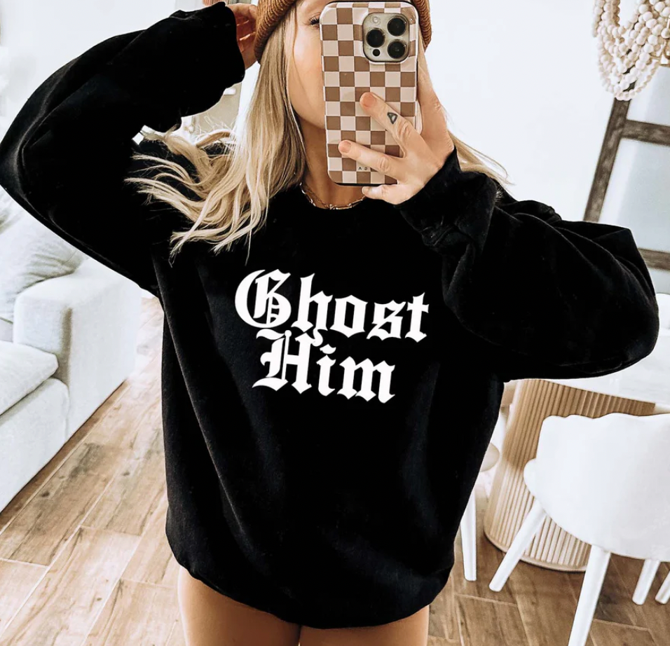 Person wearing a black sweatshirt with 'Ghost Him' text, taking a mirror selfie.