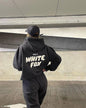 Person wearing a black hoodie with 'White Fox' text, standing against a modern architectural background.