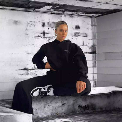 Person wearing a black hoodie and pants sitting on a concrete ledge with a distressed wall background.