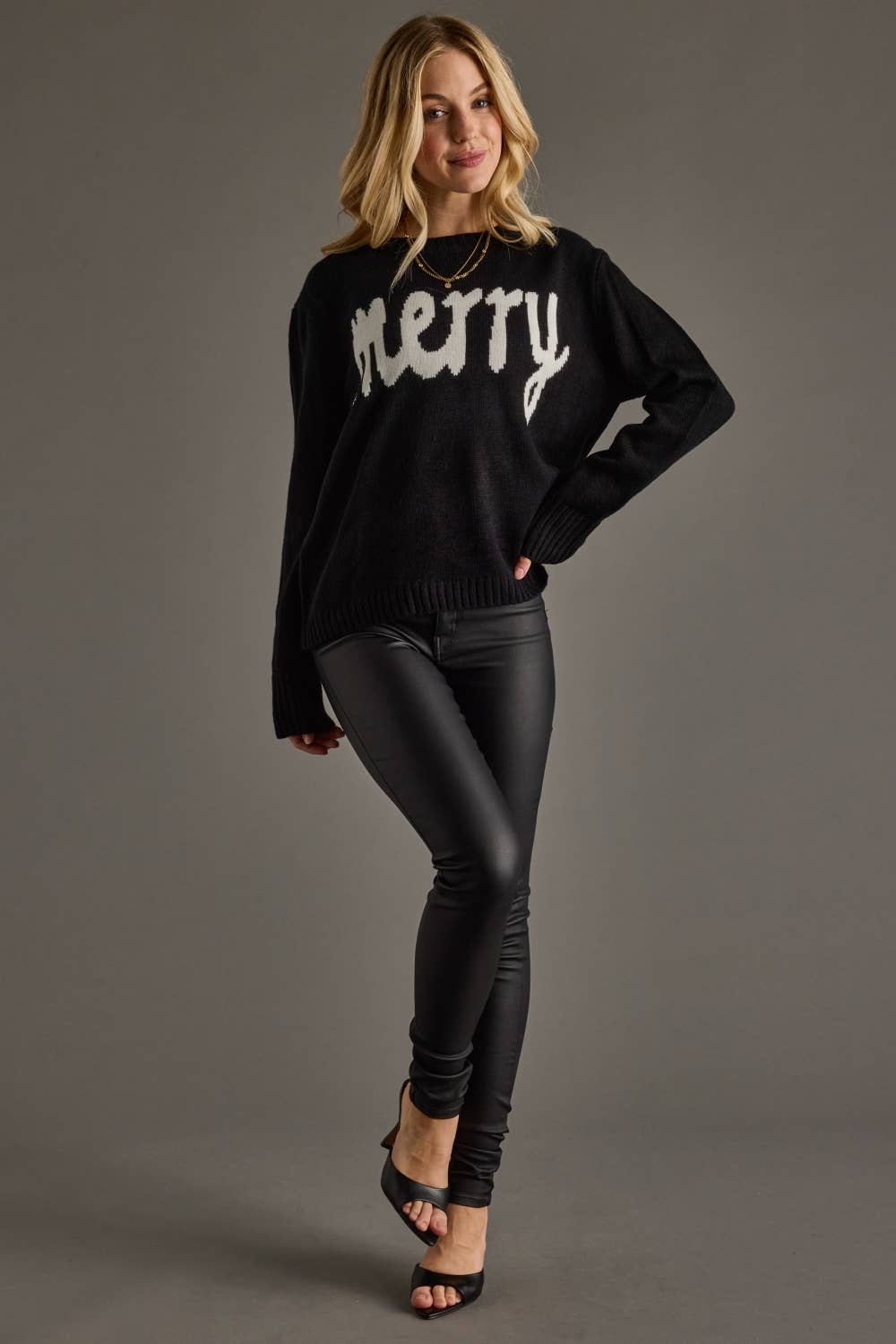 Woman wearing a black sweater with 'merry' text and black pants on a gray background