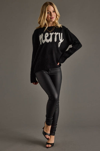 Woman wearing a black sweater with 'merry' text and black pants on a gray background