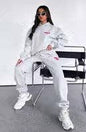 Person wearing a white tracksuit with red accents sitting on a chair.