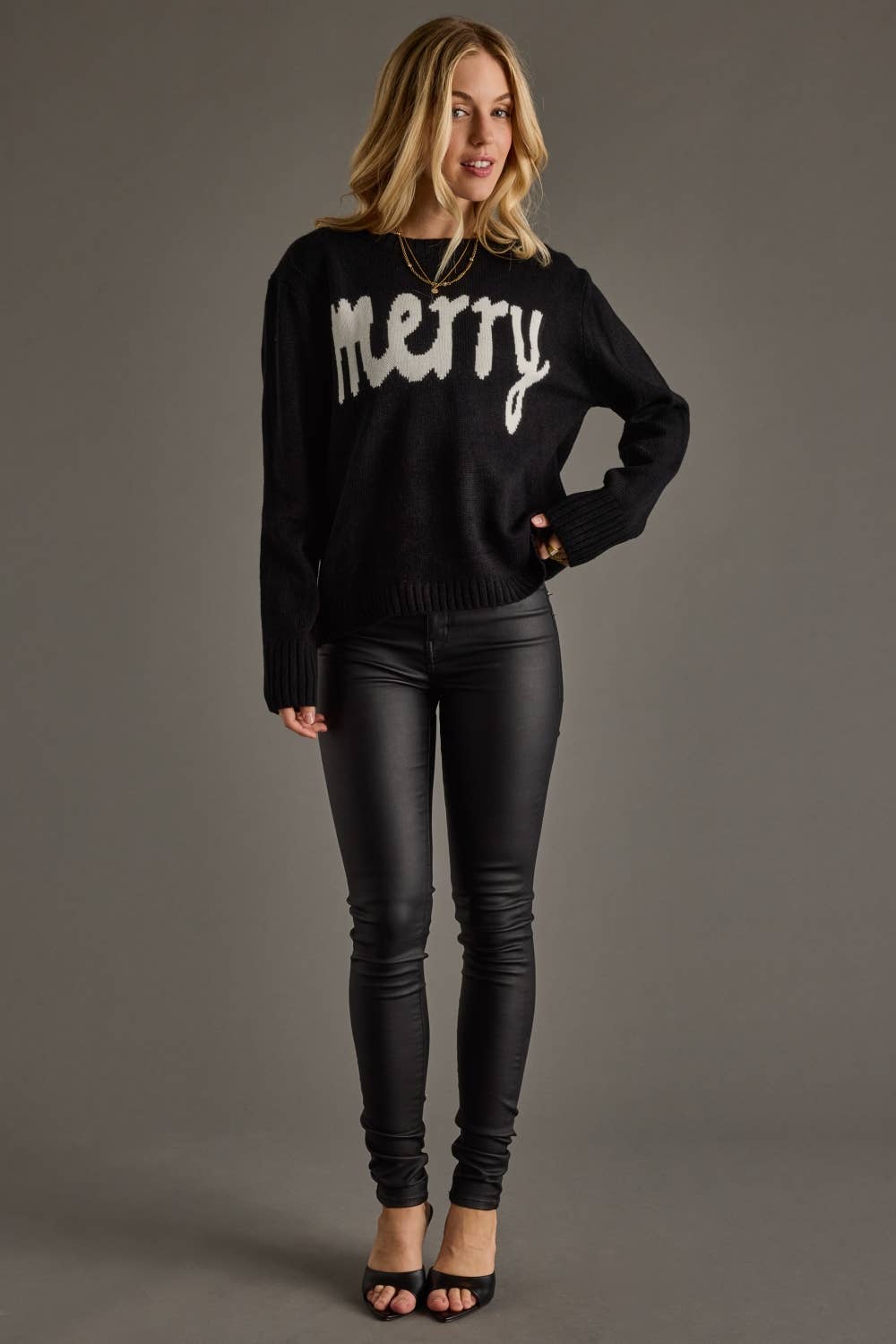 Woman wearing a black sweater with 'merry' text and black pants on a gray background