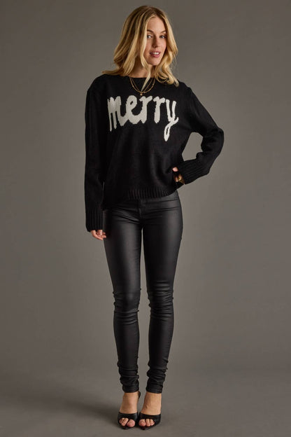 Woman wearing a black sweater with 'merry' text and black pants on a gray background
