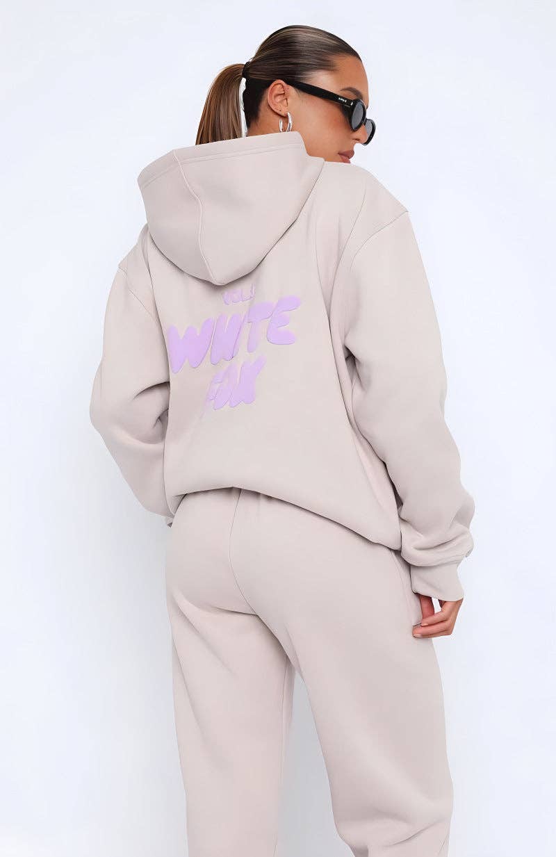 Person wearing a beige tracksuit with a logo on the back against a white background