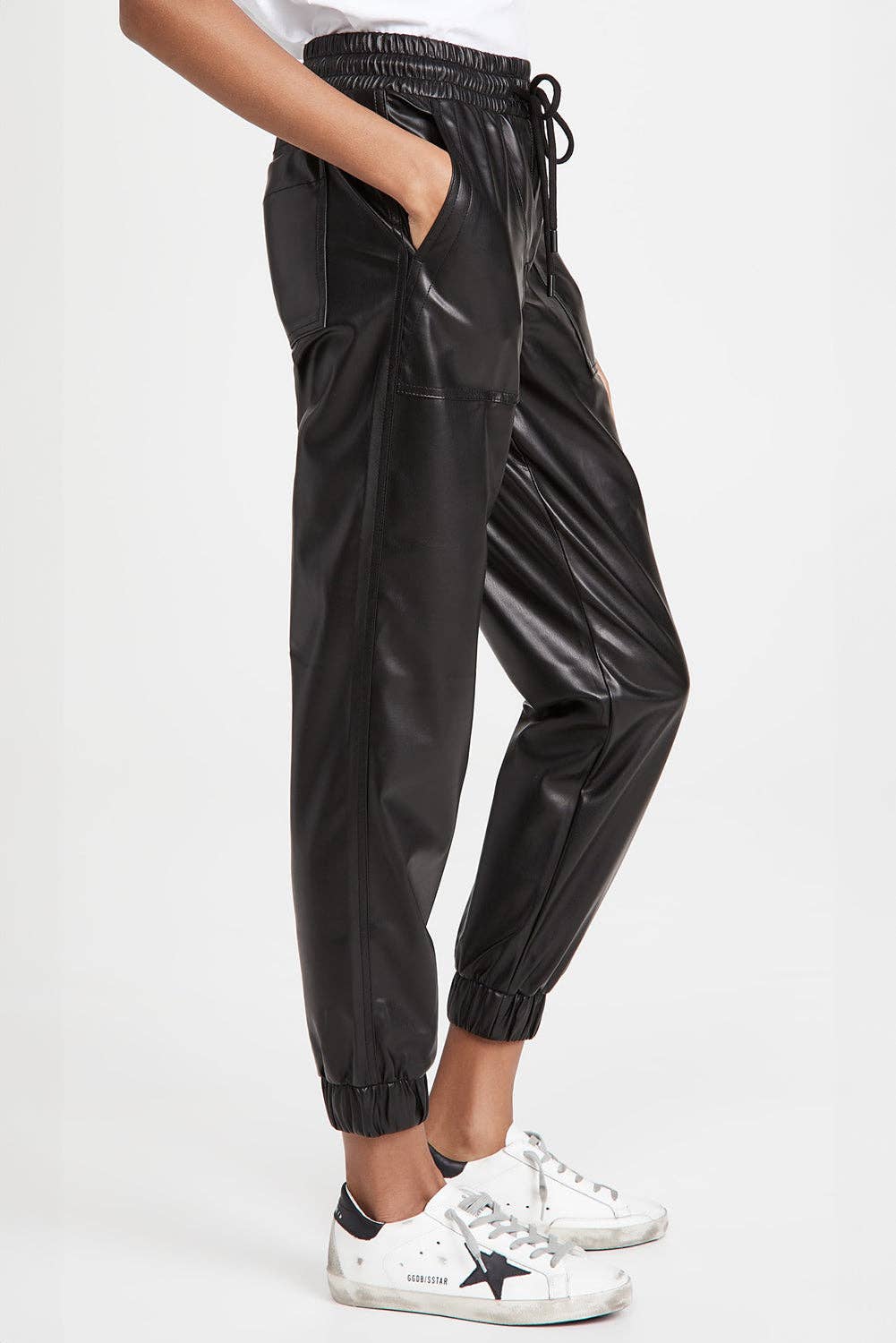 Black shiny pants worn by a person on a white background