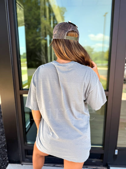 Person wearing a gray t-shirt and cap standing in front of a glass door.