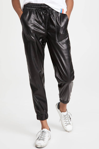 Person wearing shiny black pants and white sneakers on a white background