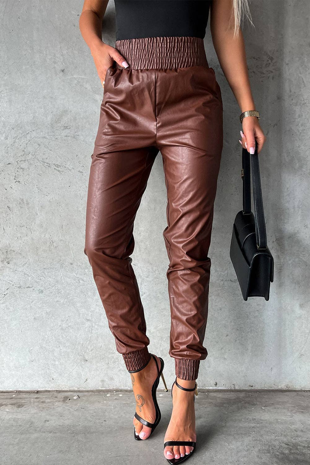 Person wearing brown leather jogger pants against a gray wall.