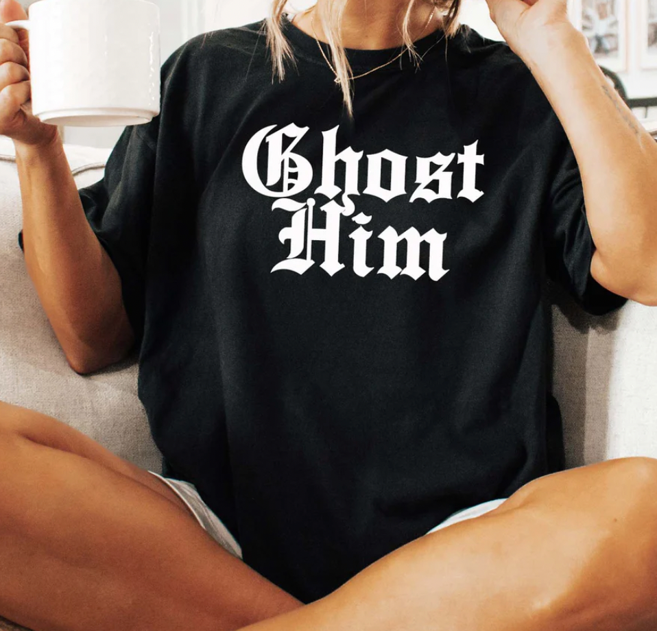 Person wearing a black t-shirt with 'Ghost Him' text, holding a white mug.