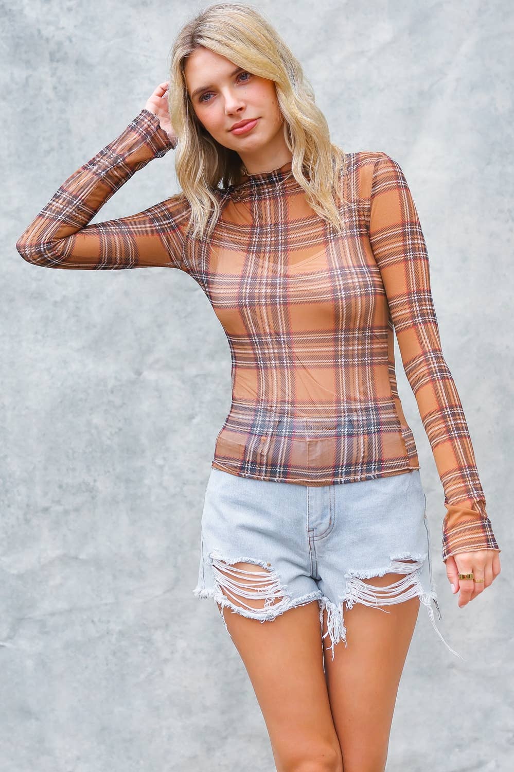 Woman wearing a plaid long-sleeve top and denim shorts against a gray background