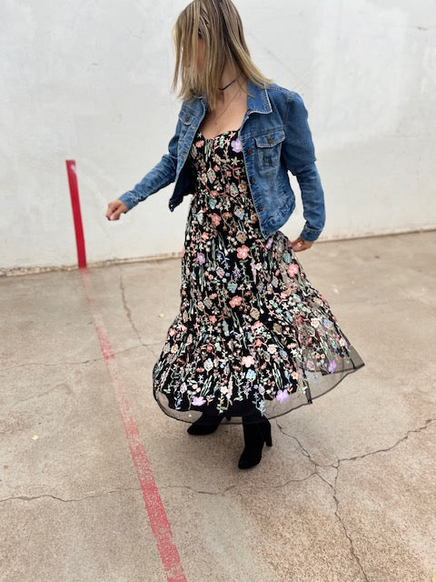Woman wearing a floral dress and denim jacket on a concrete surface.