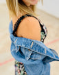 Person wearing a denim jacket over a floral dress with a blurred background