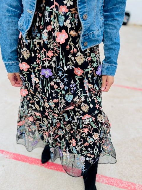 Person wearing a black floral dress with a denim jacket on a light background