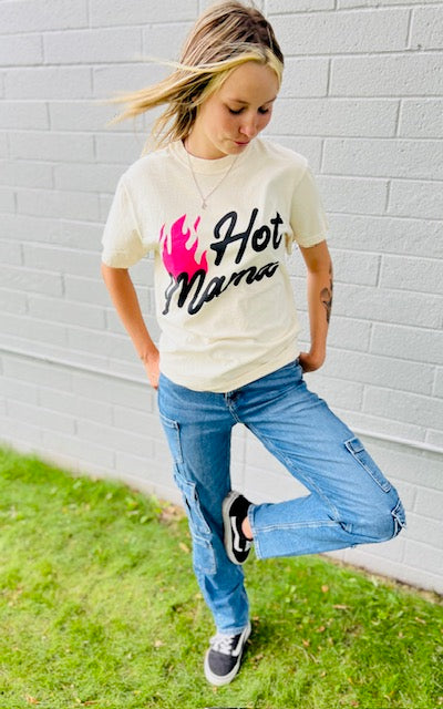 Person wearing a t-shirt with 'Hot Mama' text and graphics, standing against a gray brick wall.