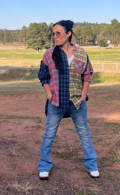 Person wearing a plaid shirt and jeans standing in an open field with trees in the background