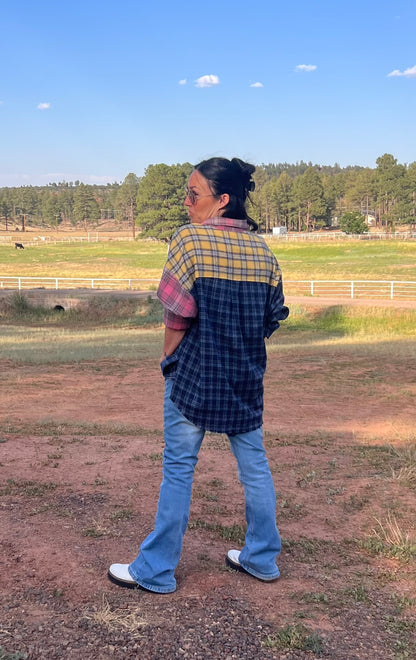 Person wearing a plaid shirt and jeans standing in an open field with trees in the background