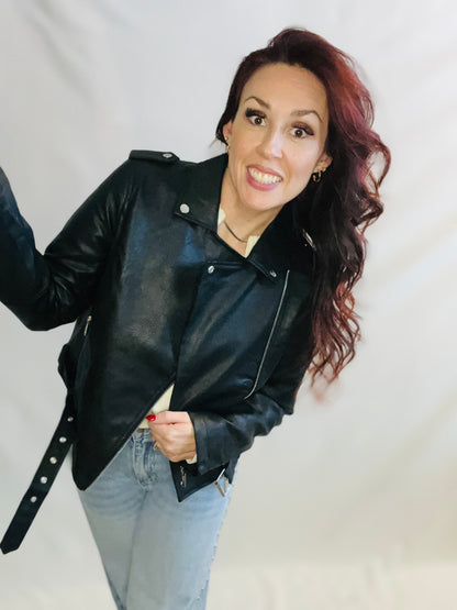 Woman wearing a black leather jacket and light blue jeans against a plain background