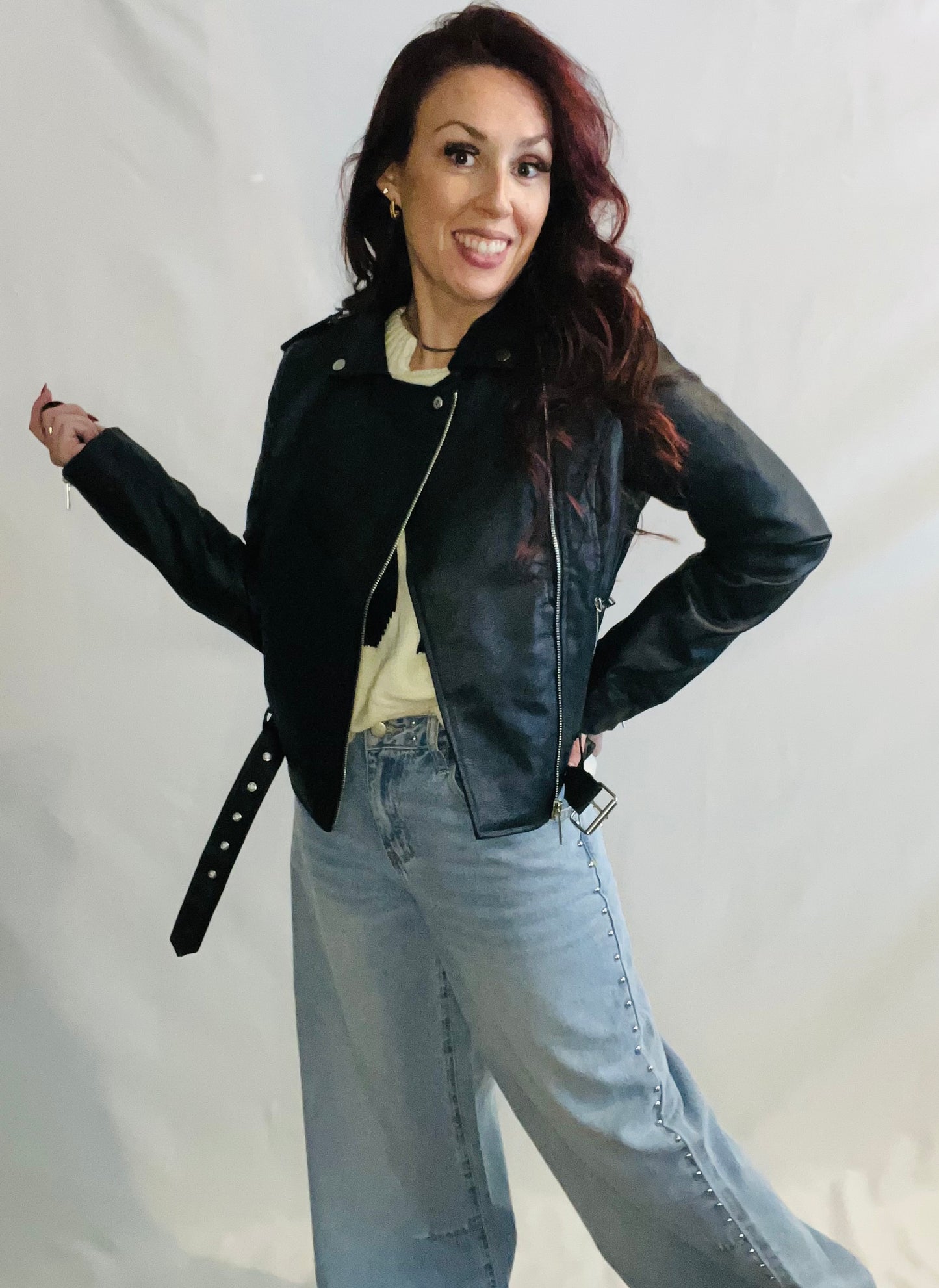 Woman wearing a black leather jacket and light blue jeans against a plain background
