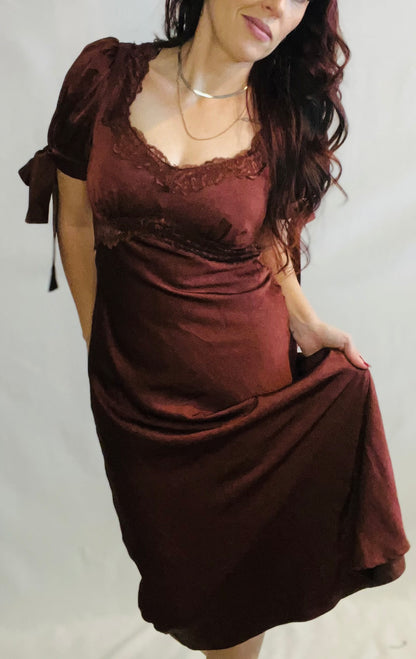 Woman wearing a brown dress with lace details on a plain background