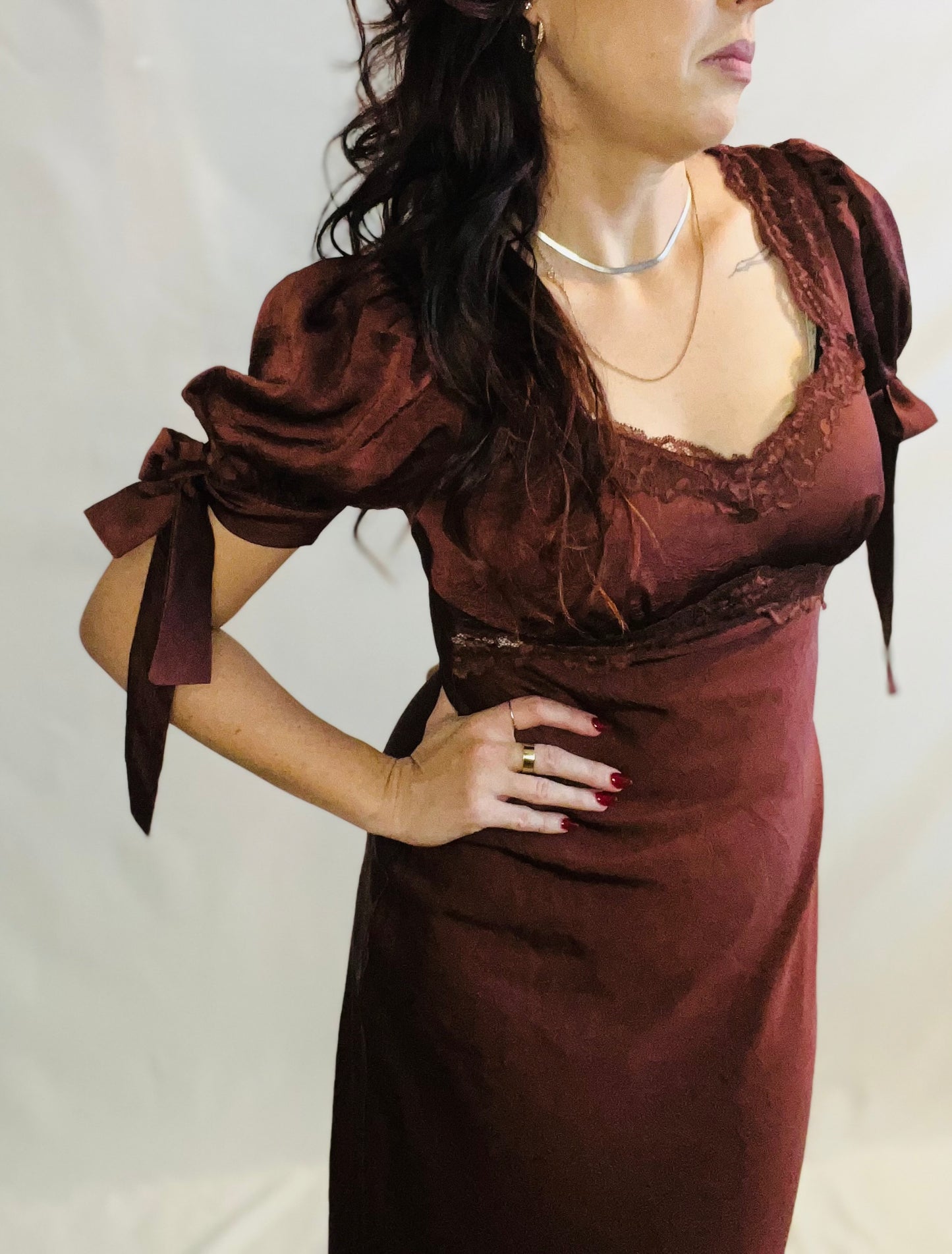 Woman wearing a brown dress with lace details on a plain background