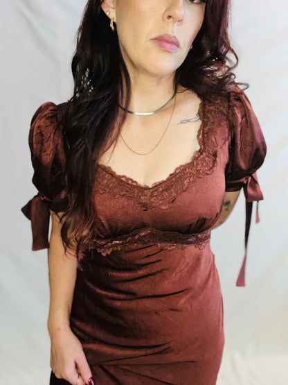 Woman wearing a brown dress with lace details on a plain background