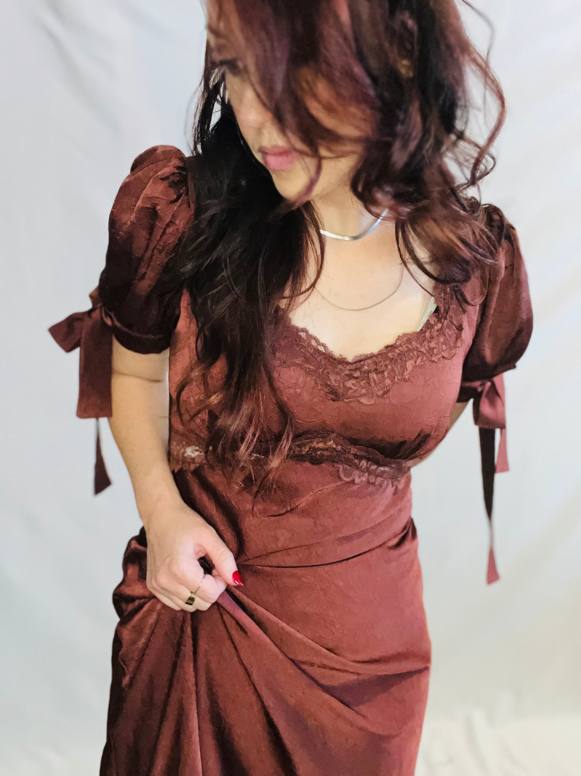 Woman wearing a brown dress with lace details on a plain background
