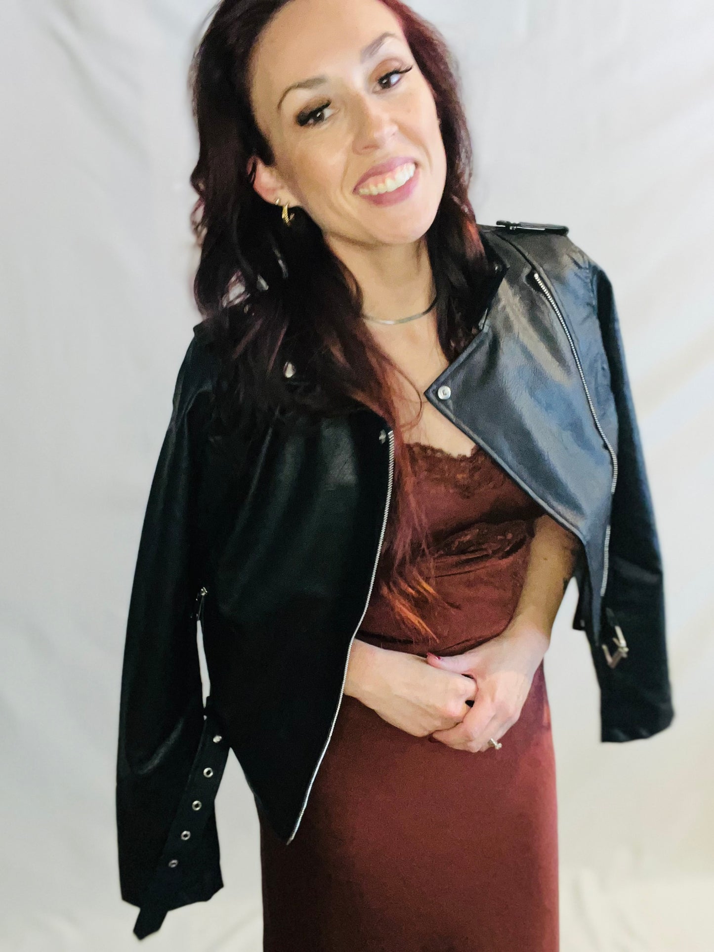 Woman wearing a black leather jacket over a brown dress on a plain background