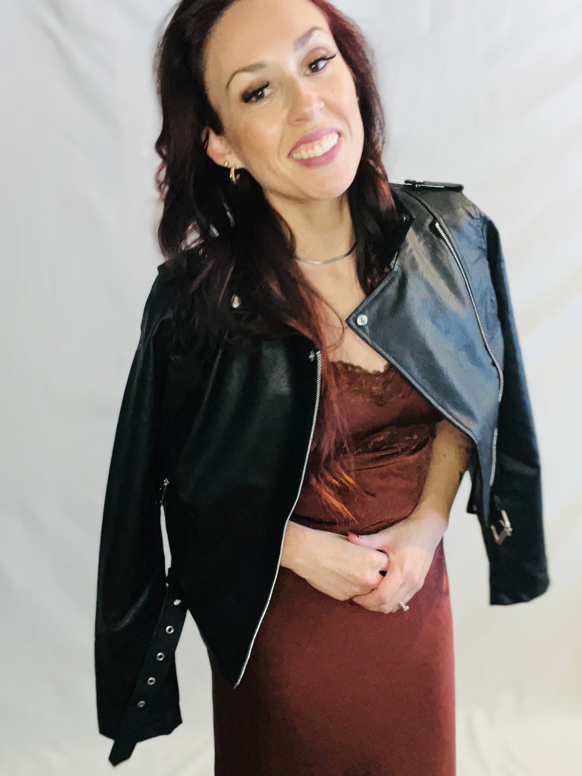 Woman wearing a black leather jacket over a brown dress on a plain background