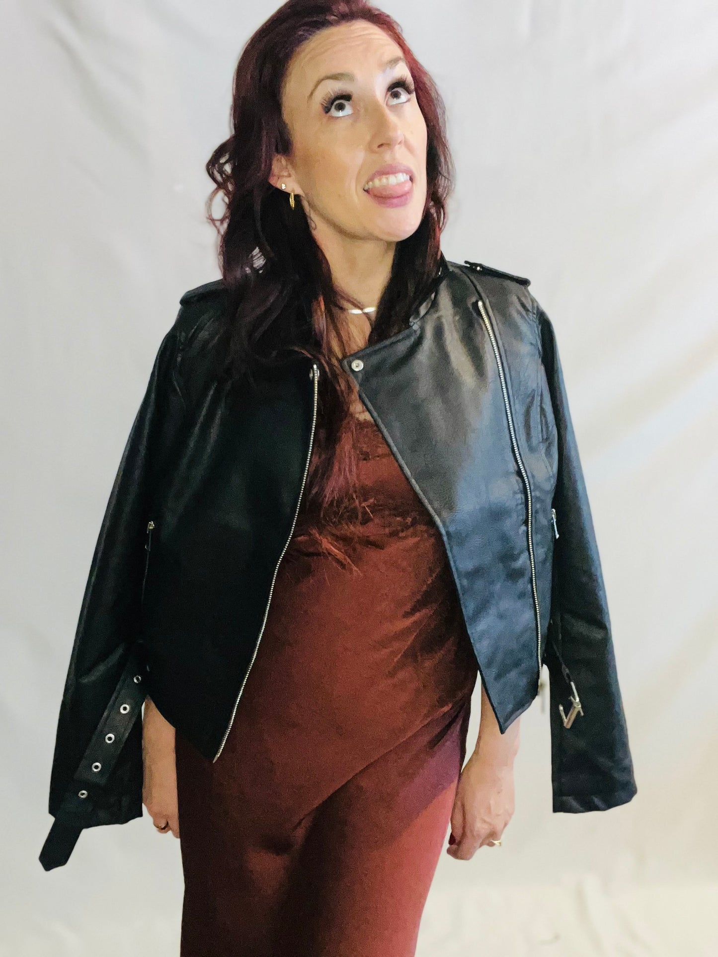 Woman wearing a black leather jacket over a brown dress on a plain background
