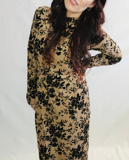 Woman wearing a beige dress with black floral pattern against a white background