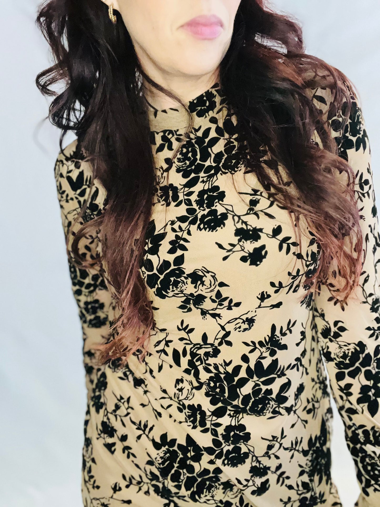 Person wearing a floral patterned top with black flowers on a beige background