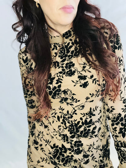 Person wearing a floral patterned top with black flowers on a beige background