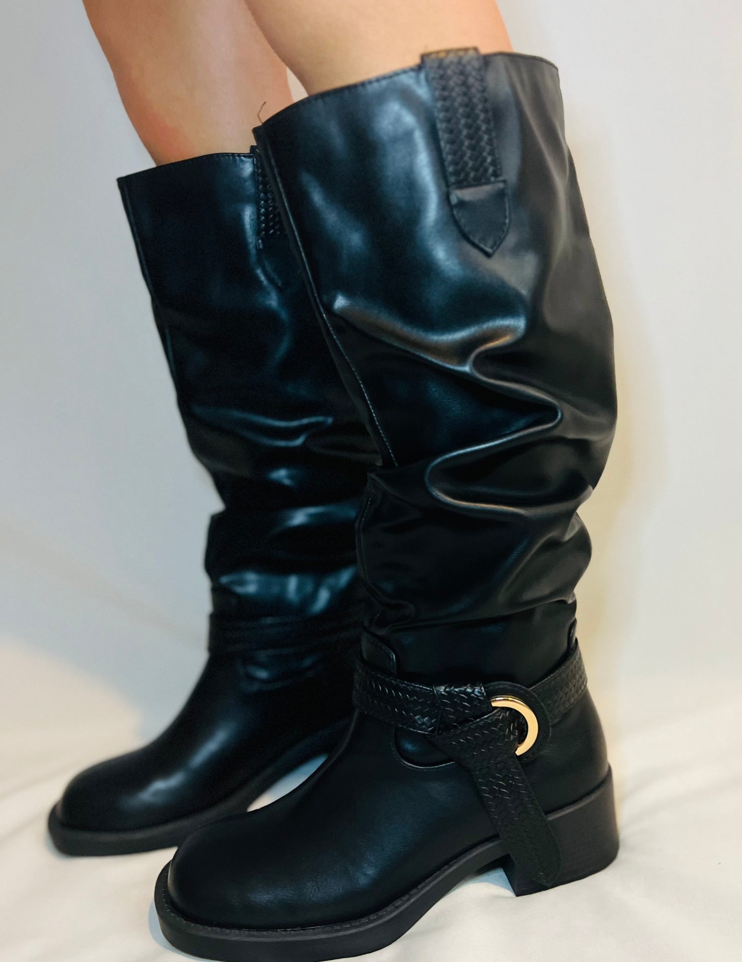 Black knee-high boots with a gold buckle on a light background