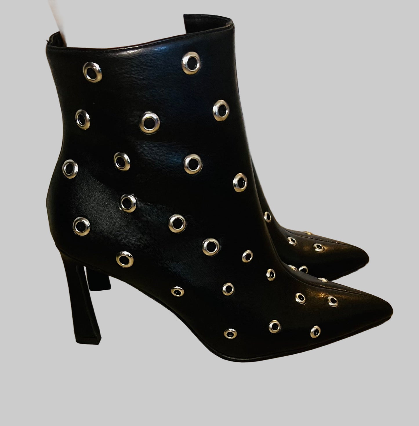 Black ankle boots with silver eyelets on a wooden floor.