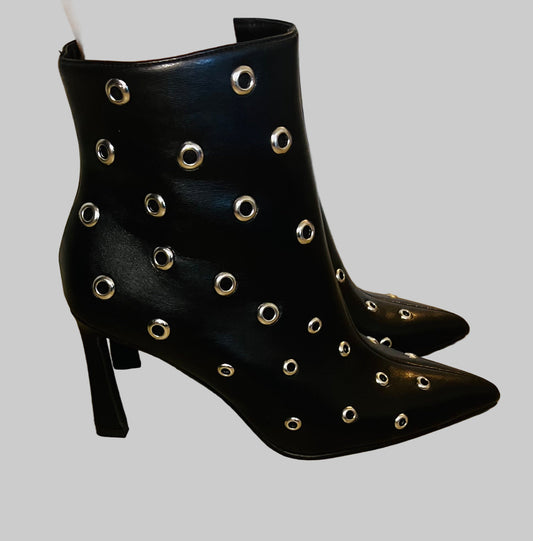 Black ankle boots with silver eyelets on a wooden floor.