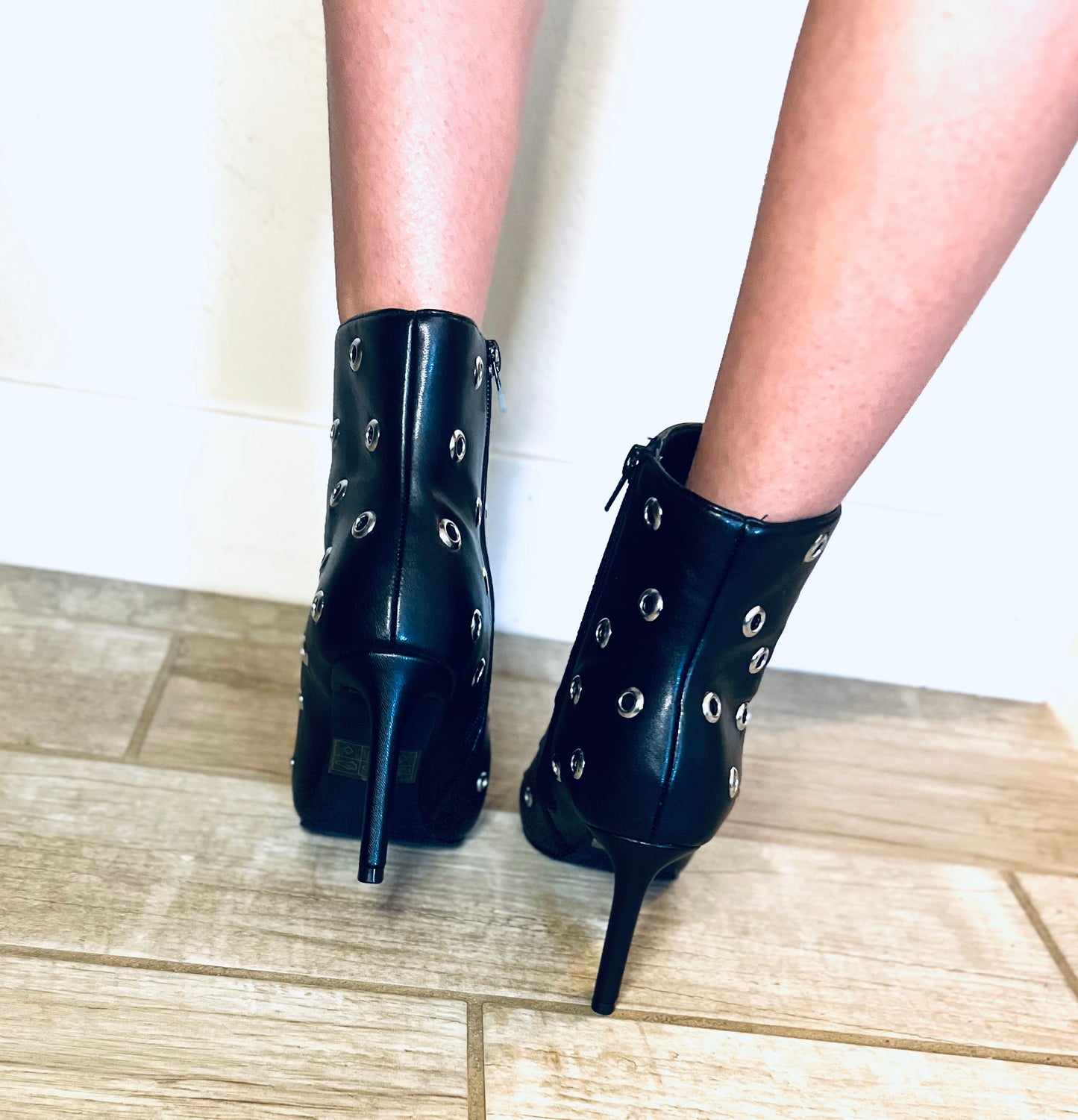 Black high-heeled boots with decorative studs on a wooden floor.