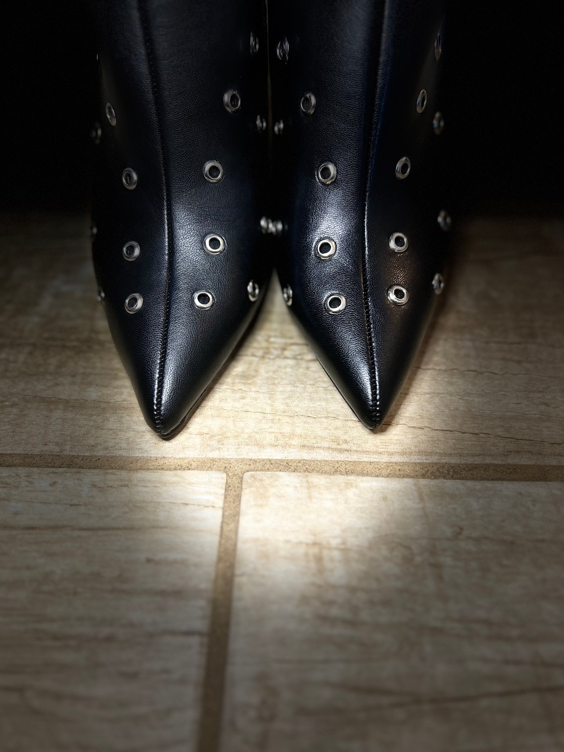 Black pointed-toe shoes with studded details on a wooden floor.