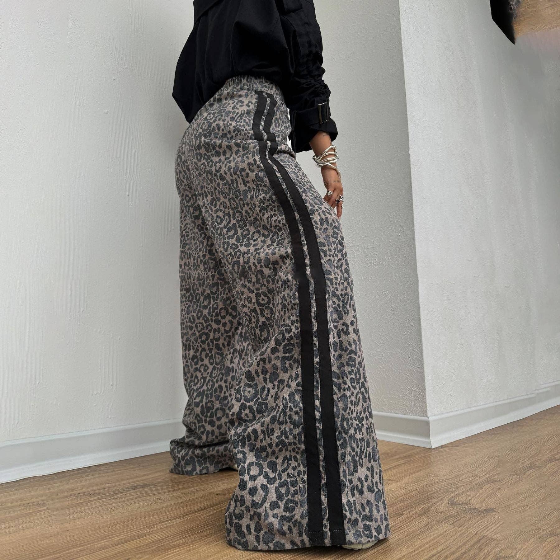 Person wearing leopard print pants with a black stripe indoors.