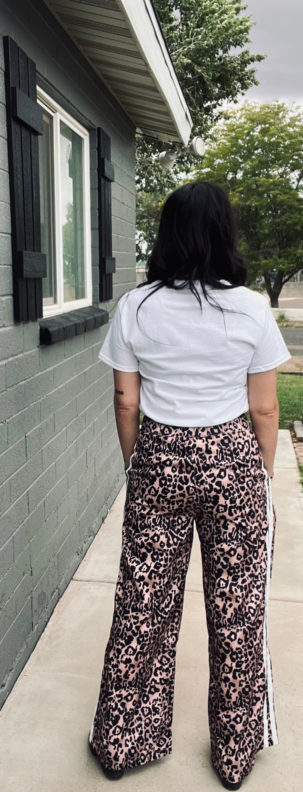 Person wearing a white shirt and leopard print pants standing on a sidewalk.