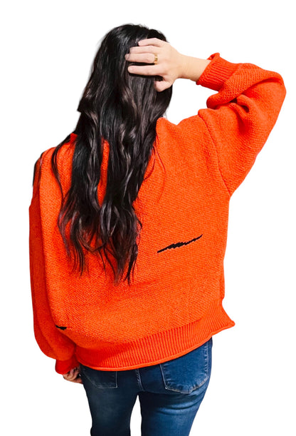 Person wearing an orange sweater with a black design on the back, standing against a white background