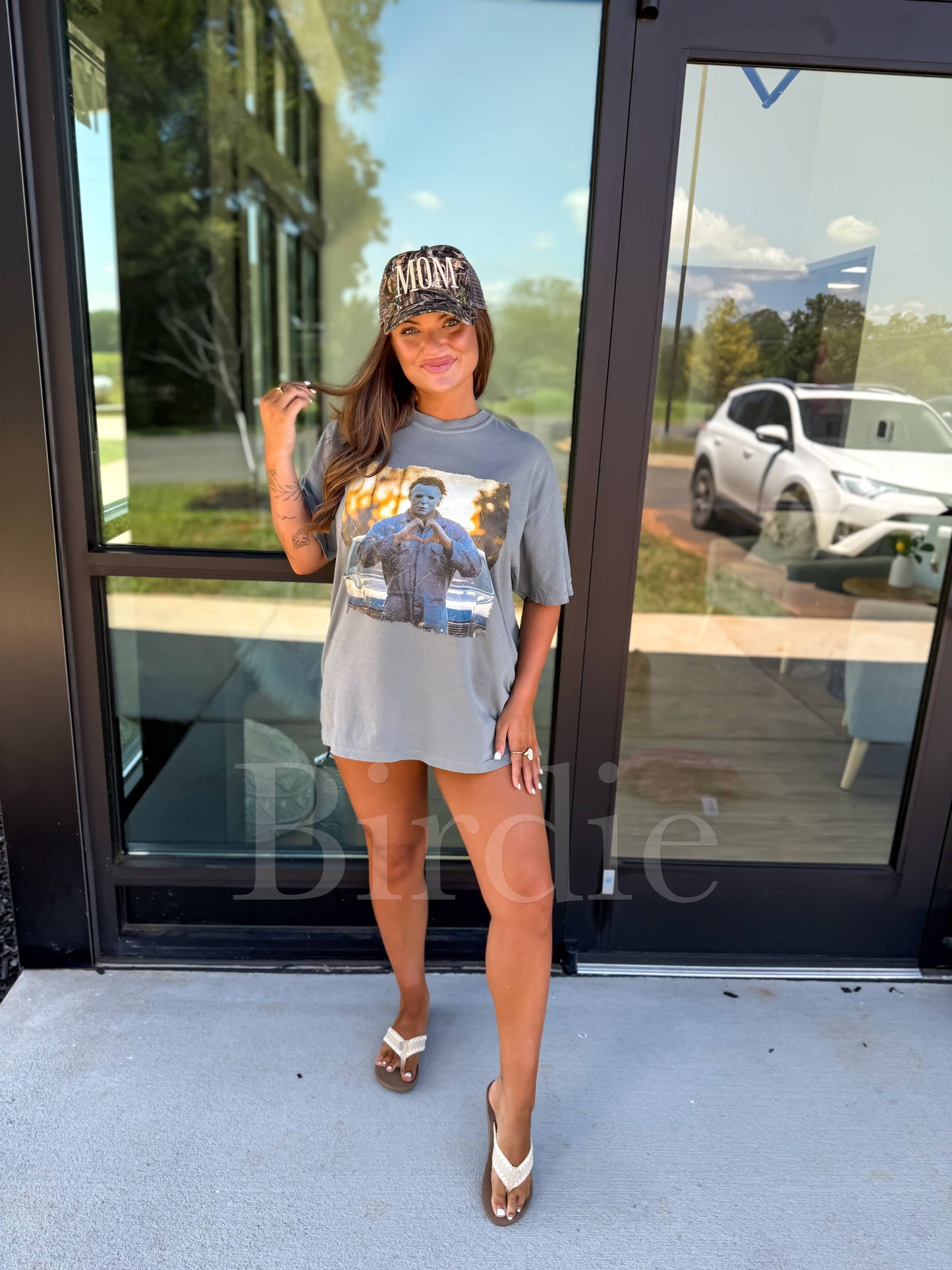 Woman wearing a graphic t-shirt and cap standing in front of a glass door.